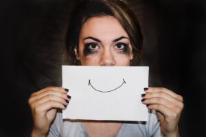 Jovem triste se escondendo atrás de sorriso desenhado.
